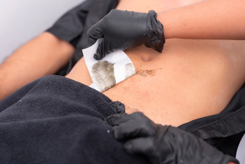 Male client receiving a professional abdominal wax at a grooming salon.
