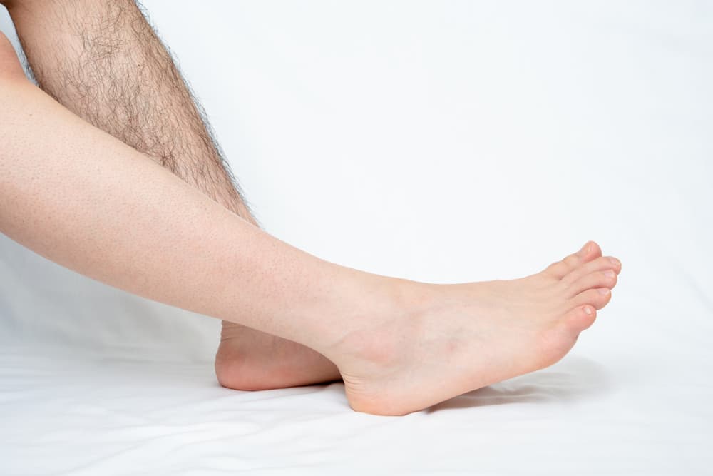 Close-up of a man’s feet and lower legs showing one side waxed and the other natural, highlighting the results of a professional men’s foot waxing treatment.