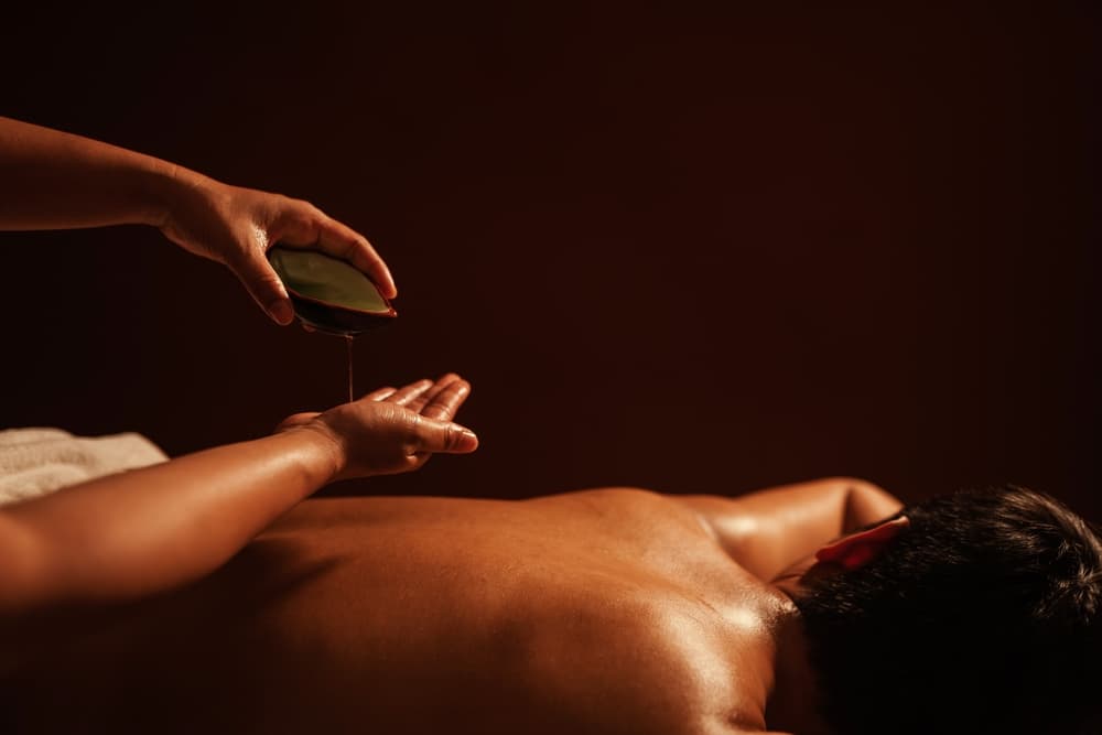Man lying face down as warm oil is poured during a close contact sensual massage in a calm, private room in Weston-super-Mare