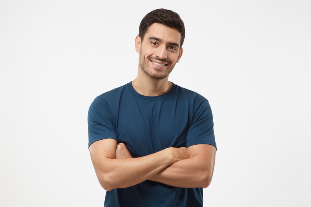 A relaxed man with smooth, hair-free lower arms standing confidently in a blue t-shirt after a professional half arm wax.