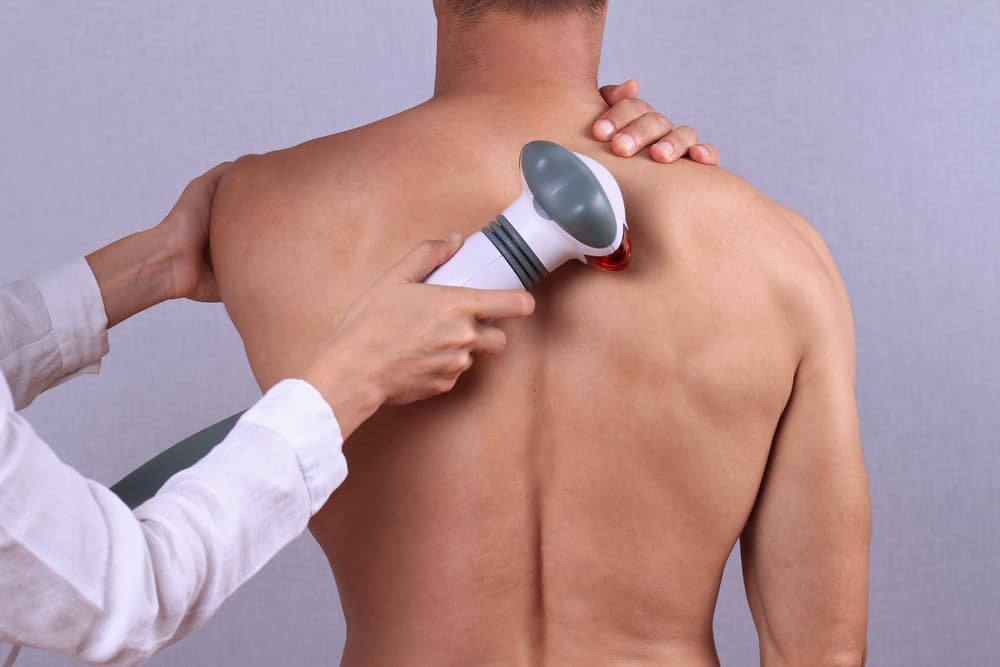 A man receiving a back massage using an infrared handheld device, designed to ease deep muscle tension. Offered at Wax and Relax, Weston-super-Mare.