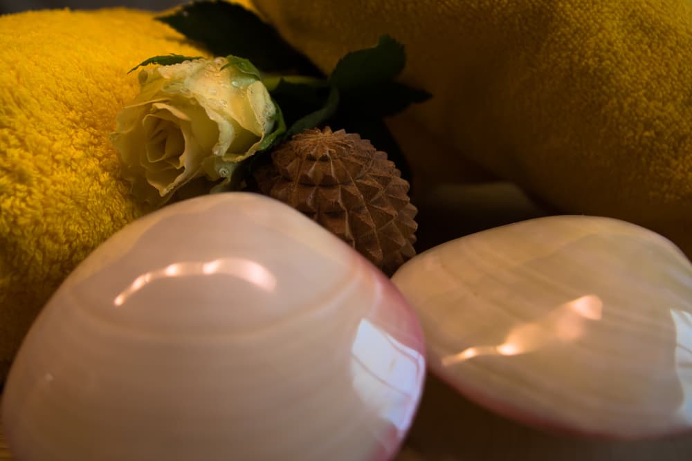 Lava shells, a yellow towel, and a fresh rose arranged in a calming spa setting. Ideal for promoting full body massage treatments with Tropic Skincare and Lava Relax.
