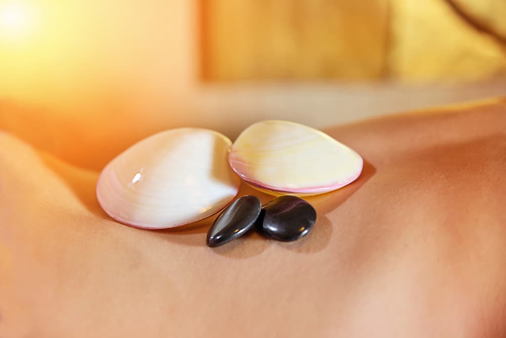 Lava shells and hot stones resting on a client’s back during a relaxing massage, representing the Lava Relax full body massage combined with Thai foot massage.