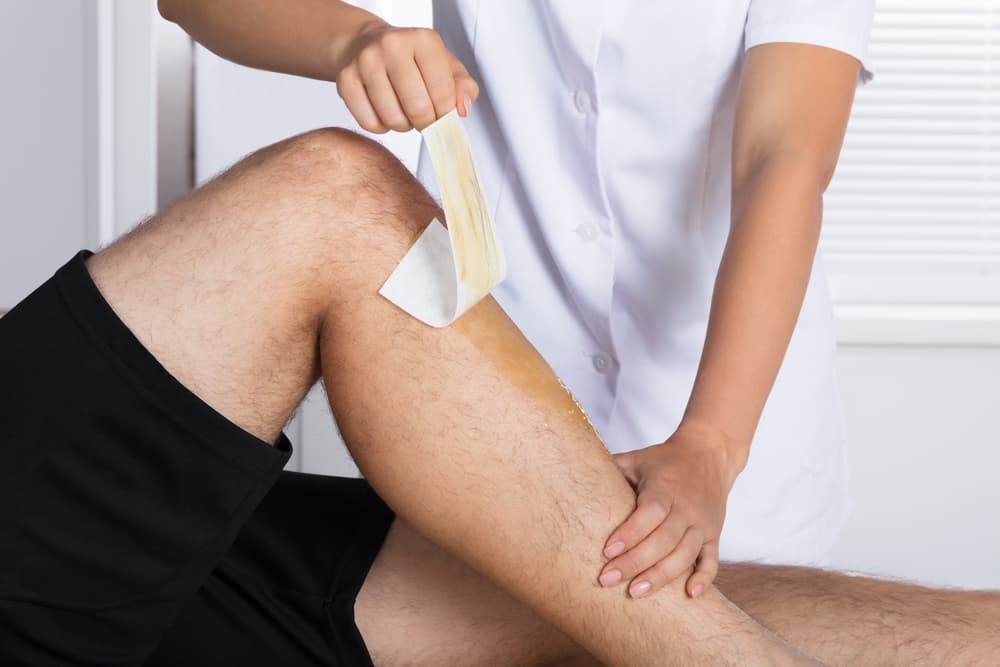 Therapist performing lower leg waxing on a male client using strip wax technique.