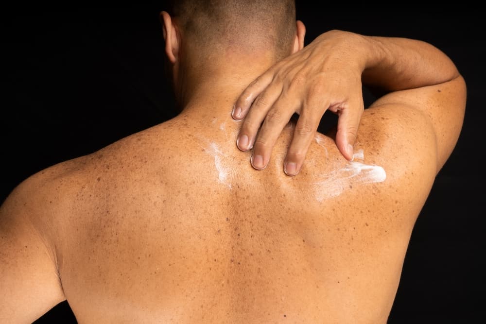 A man applying aftercare lotion to smooth, freshly waxed shoulders and upper back following a professional grooming treatment.