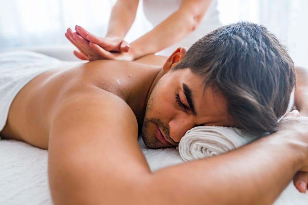 Calm male client receiving a gentle fingertip massage while lying on a massage bed.