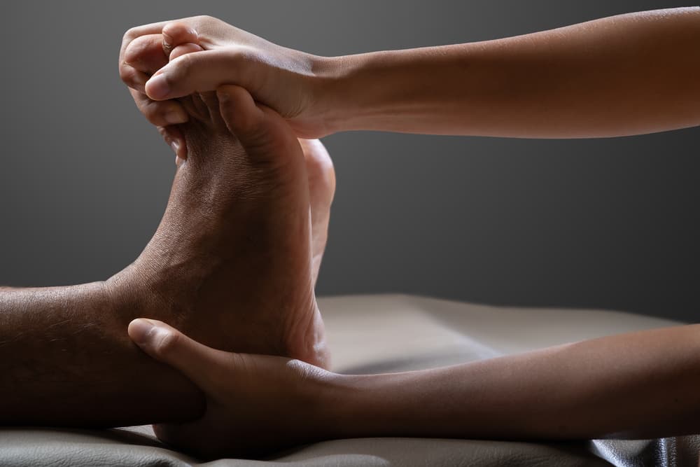 Therapist performing a Thai foot massage technique on a male client as part of a full body treatment, highlighting the stretching and pressure-based approach typical of Thai therapies.